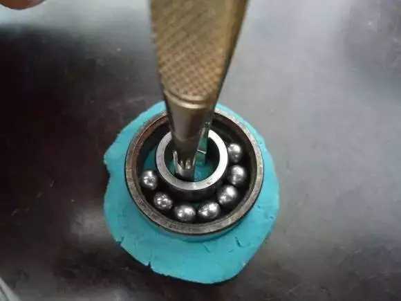 用鑷子或別的相近的物體越過內圈，同時向滾珠的方向用力頂住